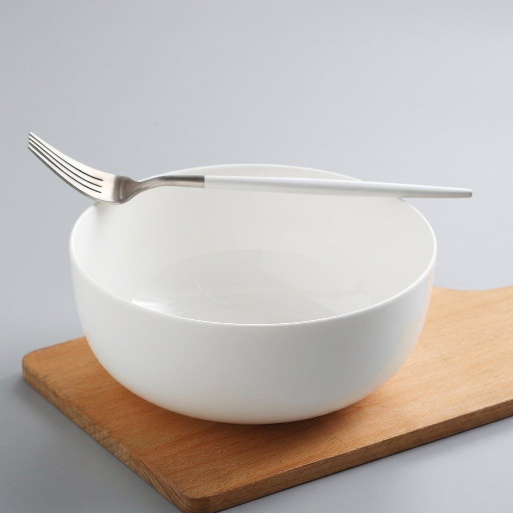 White porcelain soup bowl with fork on wooden cutting board
