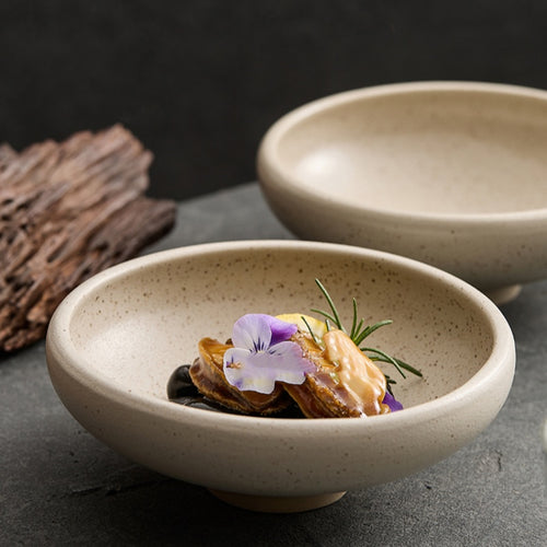 Sesame glazed ceramic conical bowl styled with edible flowers on dark slate surface
